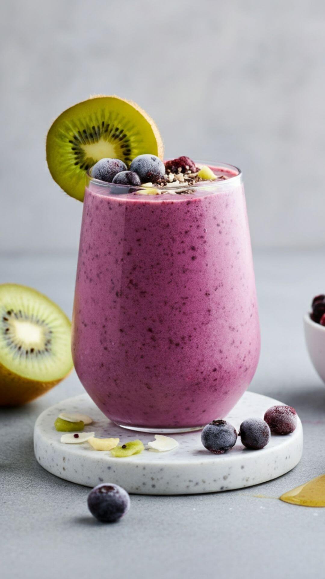A vibrant smoothie scene featuring a tall glass of Berry Kiwi Booster. The smoothie is a rich purple-pink hue, topped with a slice of fresh kiwi and a sprinkle of mixed berries. Surround the glass with ingredients: a halved kiwi, a small bowl of frozen mixed berries, and a drizzle of honey. The background is light and fresh, evoking a healthy, refreshing vibe.