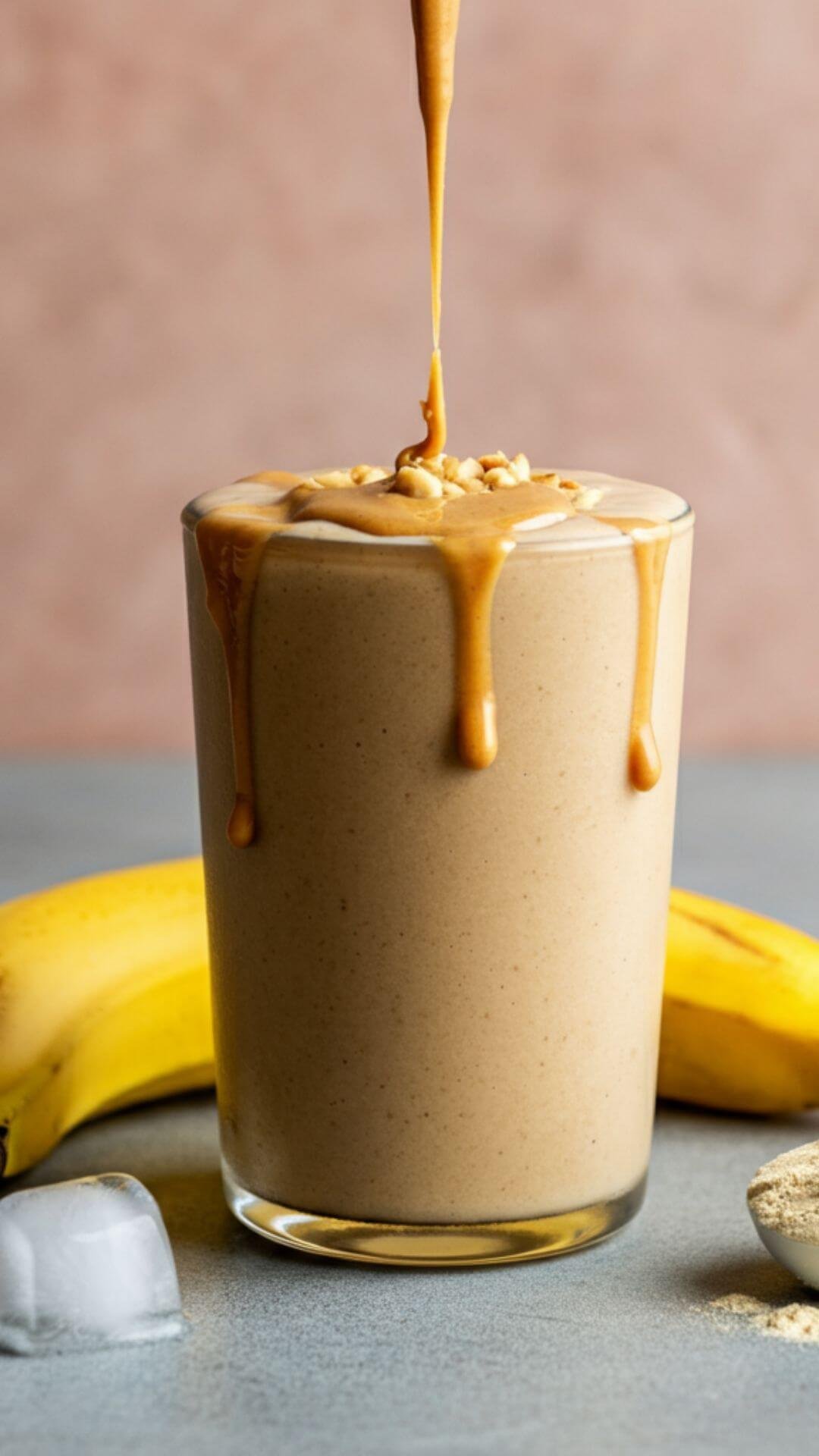 Create a bright, appetizing image of a creamy banana peanut butter smoothie in a clear glass. Include a ripe banana alongside a small jar of natural peanut butter, and a scoop of protein powder on the side. Add a few ice cubes scattered around for a fresh touch. Style the image with a clean, minimalist background, and ensure the smoothie looks rich and silky, topped with a light drizzle of peanut butter or a sprinkle of crushed nuts.