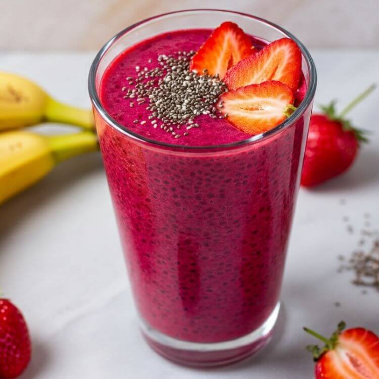 A vibrant and colorful smoothie in a clear tall glass, topped with fresh strawberries and a sprinkle of chia seeds. The smoothie is a rich, deep pink color from the beetroot and strawberries, with a soft, inviting texture.