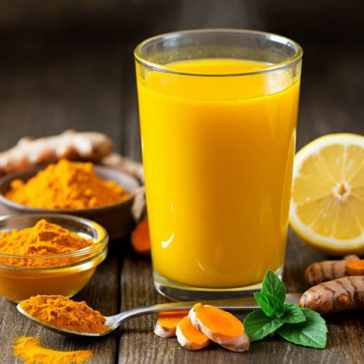 A cozy fclose-up of a warm turmeric tonic setup: a tall glass of golden yellow drink steaming slightly